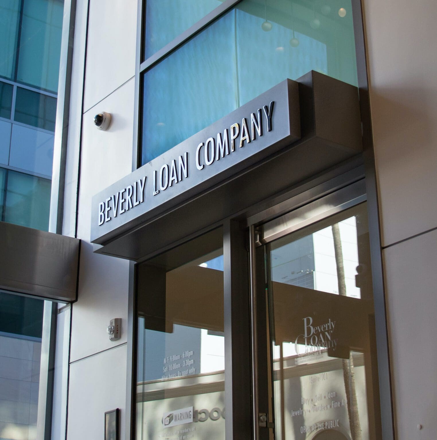 Entrance to Beverly Loan Company in Beverly Hills, with a brushed-steel BEVERLY LOAN COMPANY sign above a glass door inside a high-end office building.