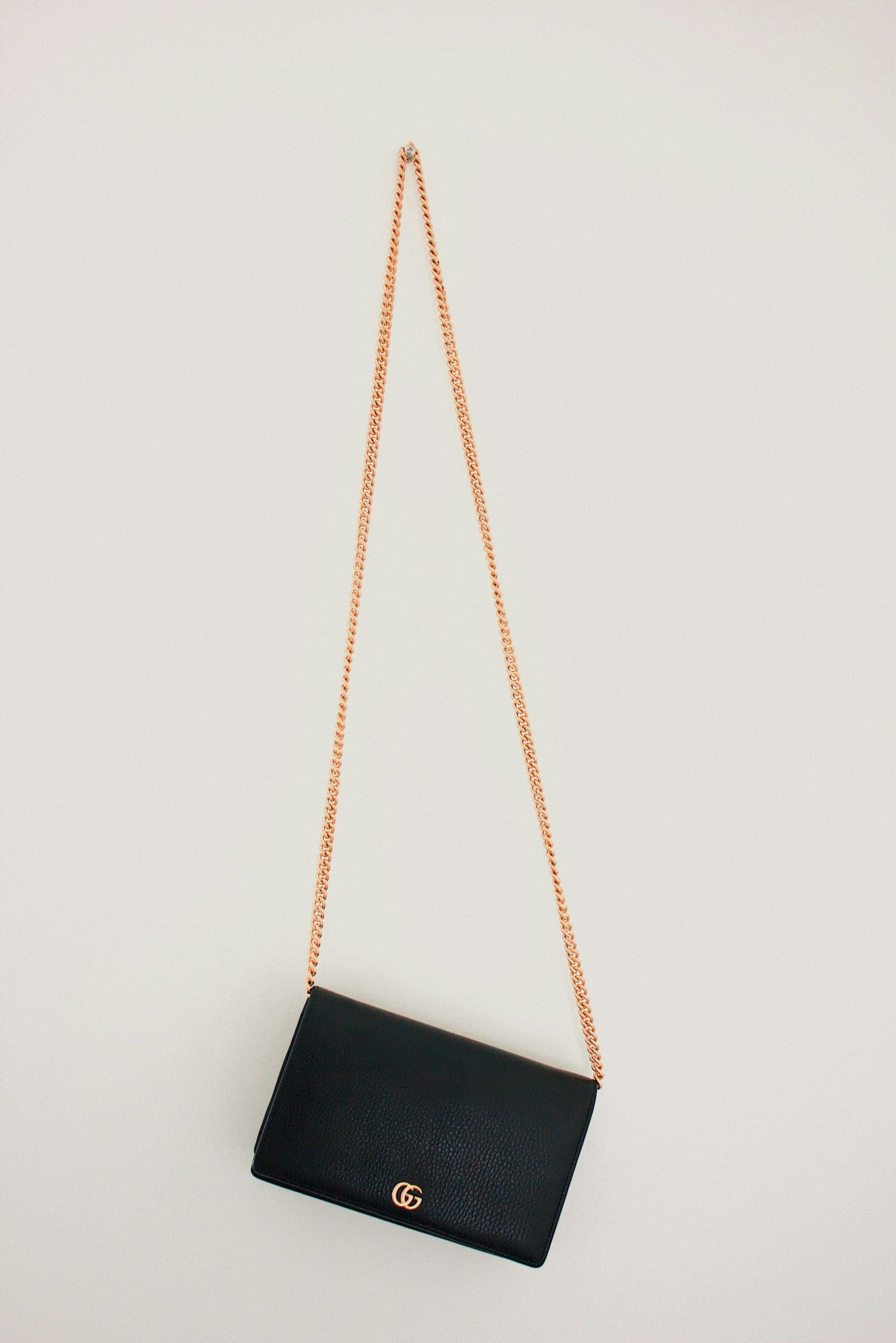A black leather Gucci wallet on a chain hangs against a white wall.